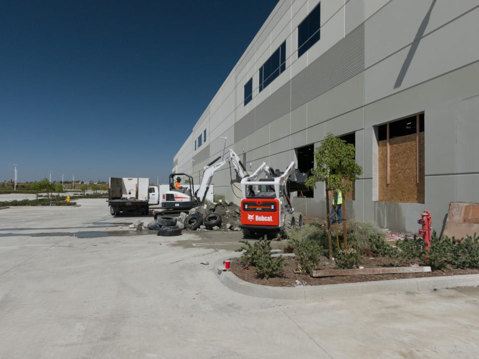angle view of two technicians in bobcats demolishing concrete slabs from wall saw openings at ups facility in riverside, ca