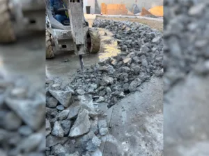 Close up view of Bobcat with hydraulic breaker firing its chisel point into the concrete at Vans Skatepark in Costa Mesa