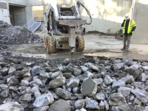 Front view of Bobcat with hydraulic breaker firing its chisel point into the concrete at Vans Skatepark in Costa Mesa