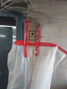 Red tape and plastic sheeting attached to a cinder block wall marked for concrete chain sawing